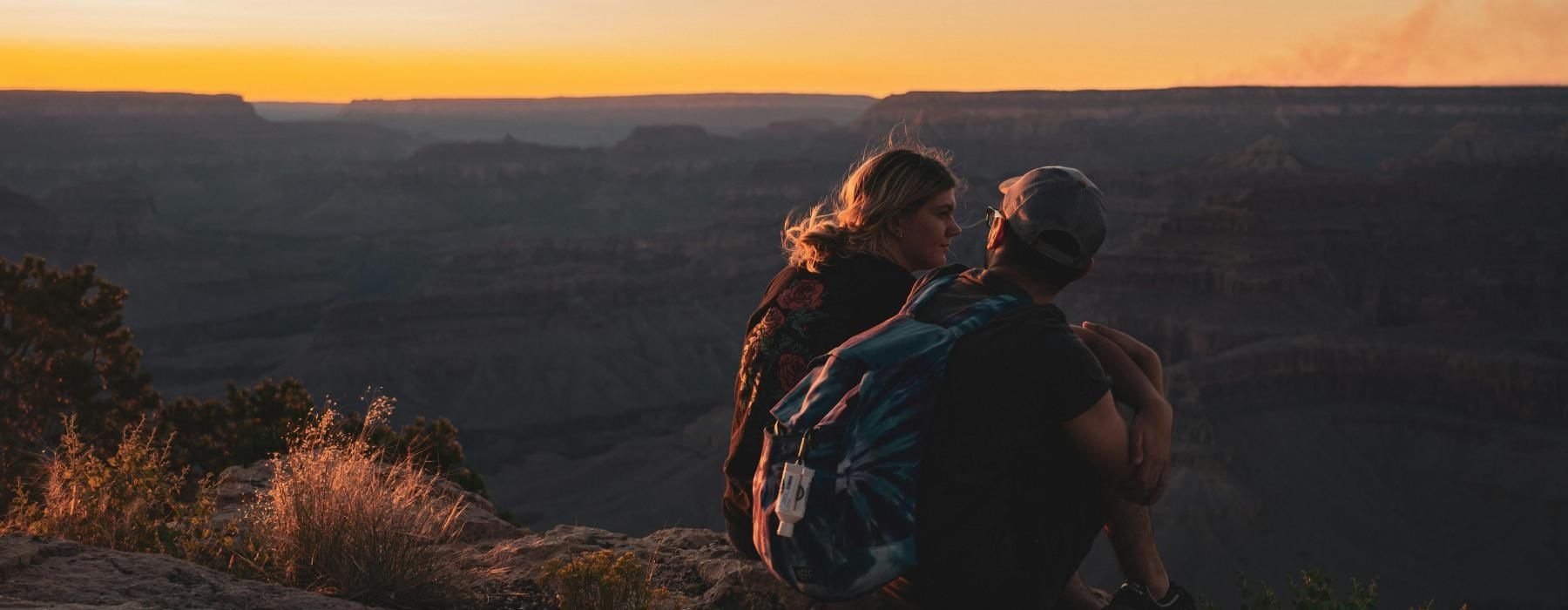 a man and woman sitting on a rock overlooking a valley