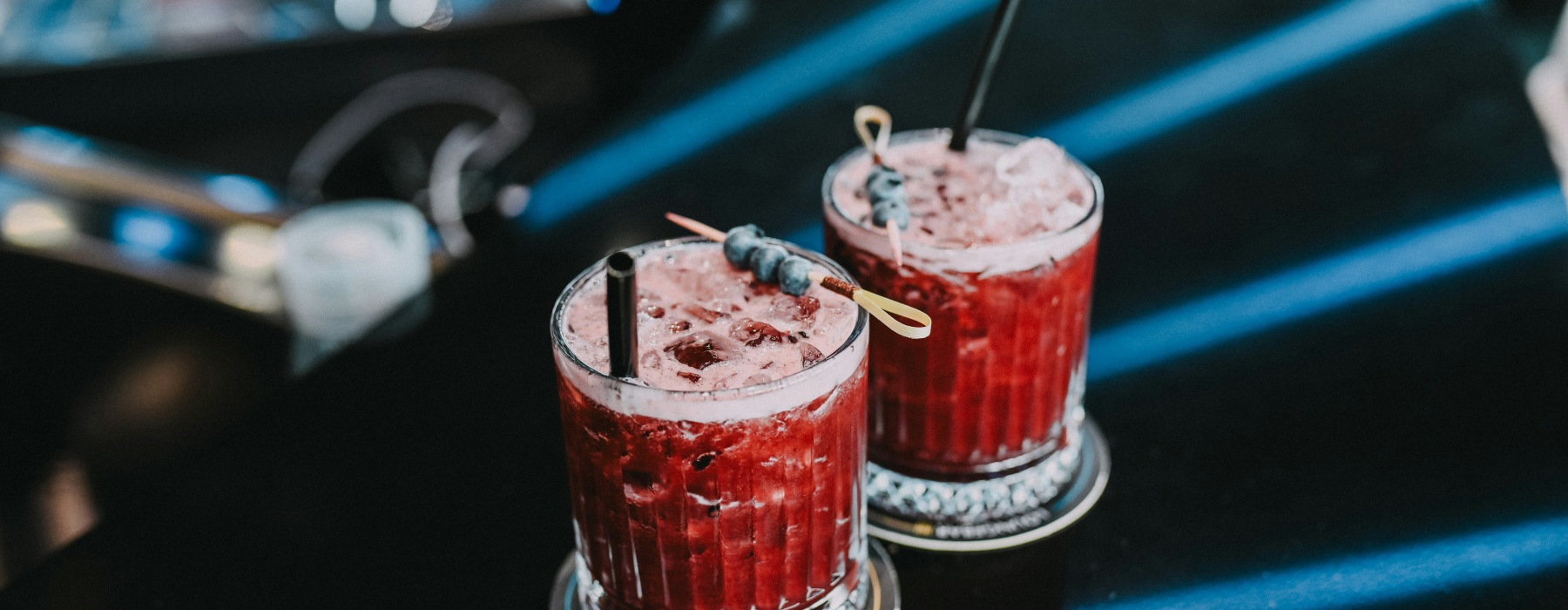 Two red berry cocktails with blueberries served on a dark bar.