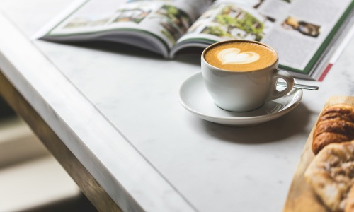 Remote work setup in a Las Vegas coffee shop with a cup of latte, open magazine, and pastries on a table.